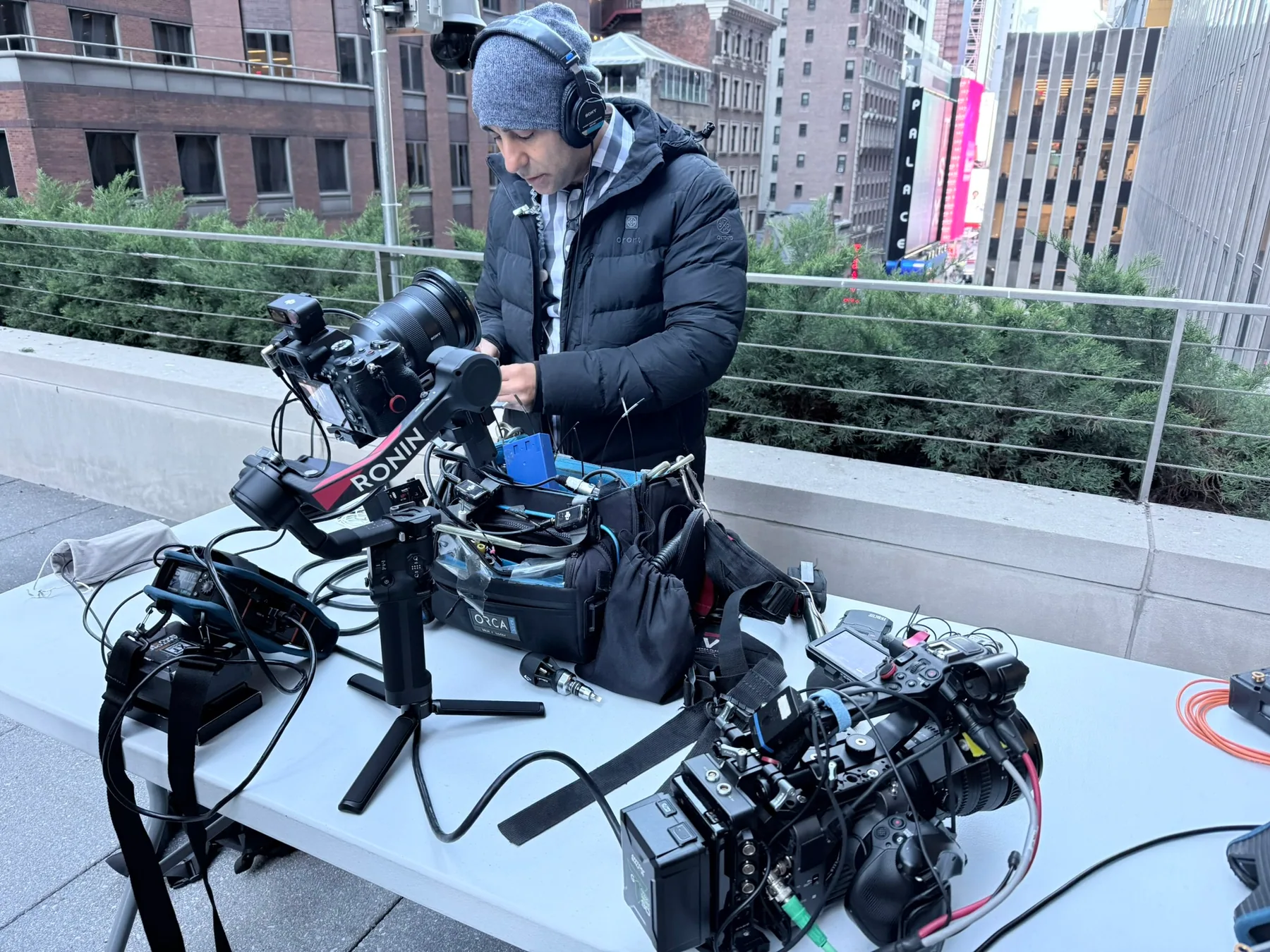 Matthew Legreca preparing audio gear beside cameras on an exterior city rooftop