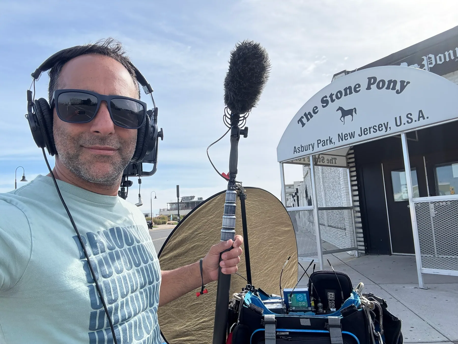 Matthew Legreca with headphones, boom, reflector, and field audio bag outside a venue